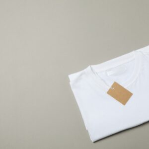 Folded blank white t-shirt with tag on gray background, space for text