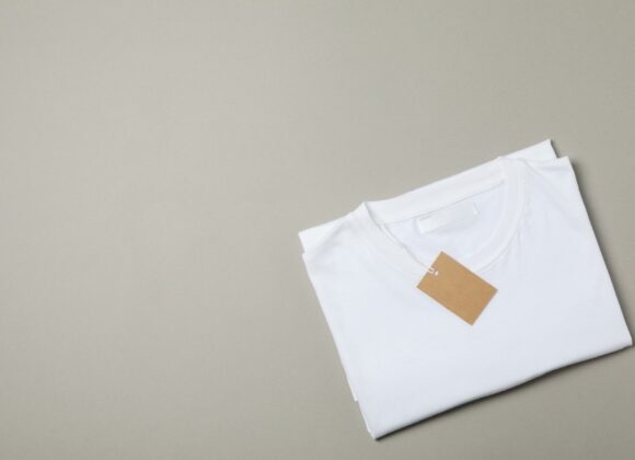 Folded blank white t-shirt with tag on gray background, space for text