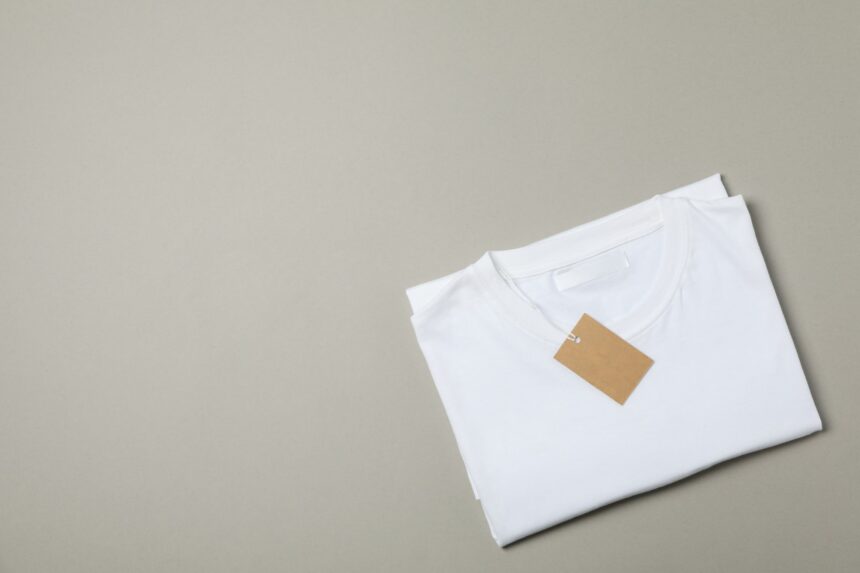 Folded blank white t-shirt with tag on gray background, space for text